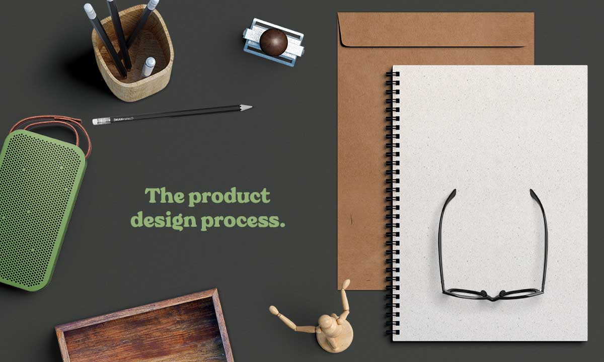 Title image for 'The product design process' with a notebook, pencils and glasses on a dark desk